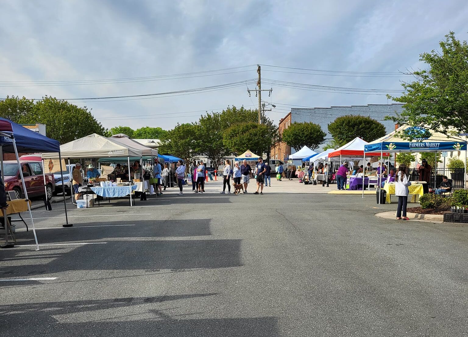 Outdoor market with multiple vendor tents and people browsing under a partly cloudy sky.