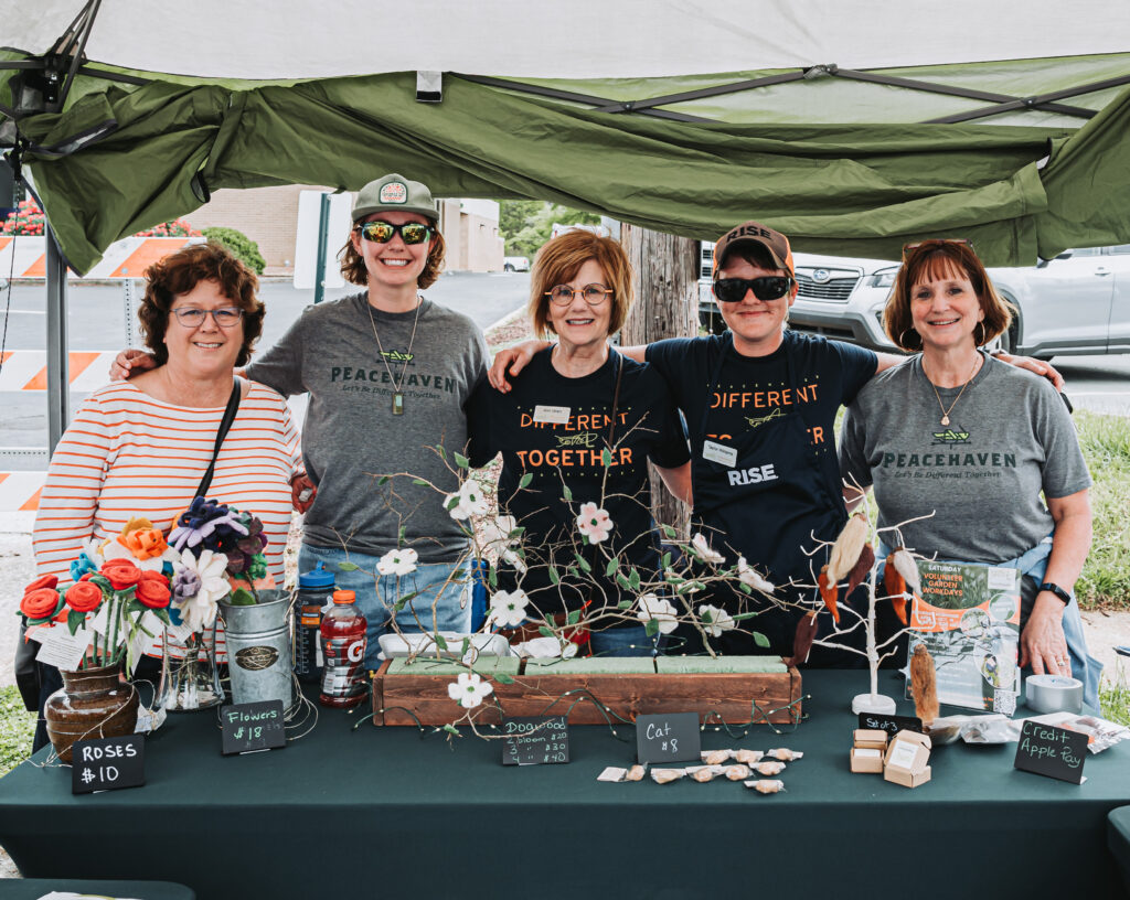 Five people standing and smiling at a booth at the dogwood festival with flowers covering the table