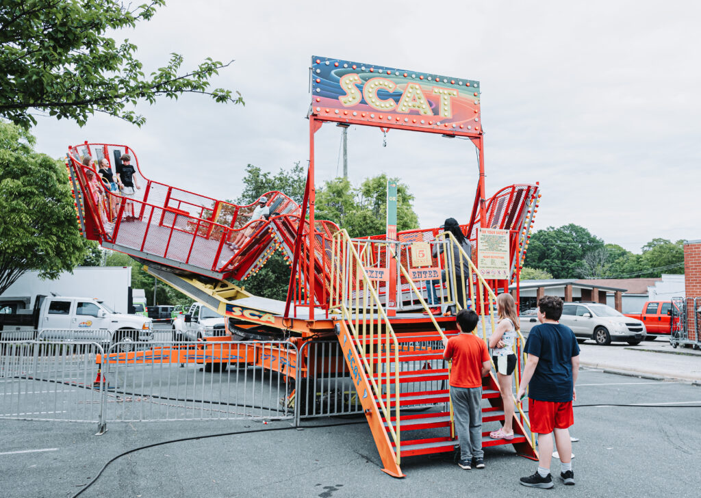 Picture of carnival ride "Scat" in a parking lot with kids on the ride and kids waiting in line for the ride