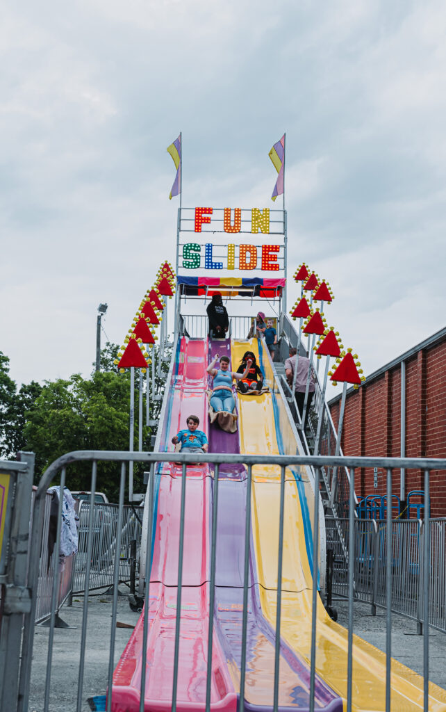 Outdoor image of the carnival attraction the fun slide with slides colored purple pink and yellow. Kids riding down the fun slide