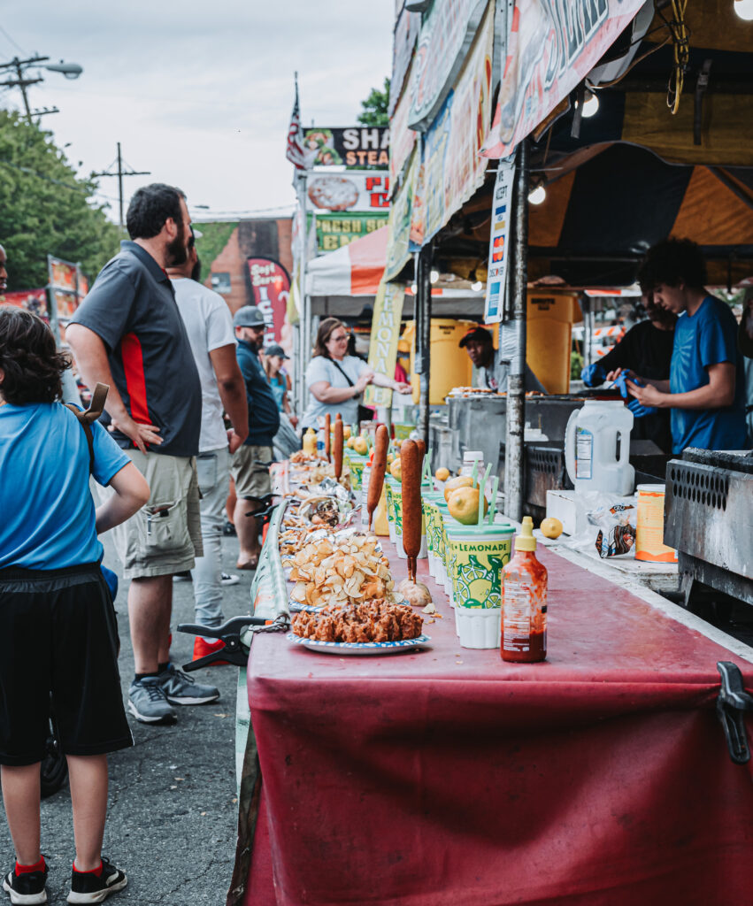 Outdoor food stations with an array of food from lemonade to corn dogs to funnel cakes with people lined up to get food