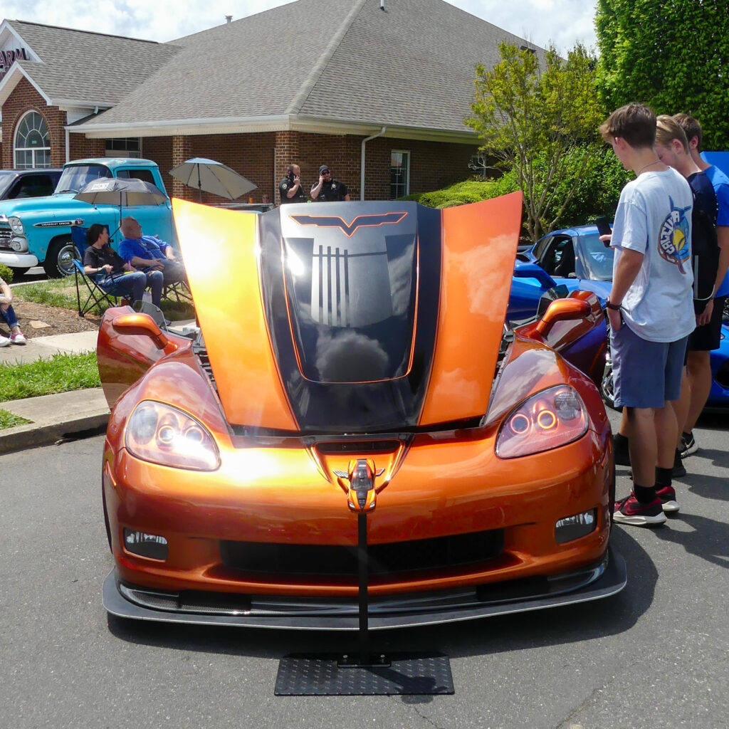 image of orange car with black stripe on the hood at mebane dogwood car show with people standing around it 