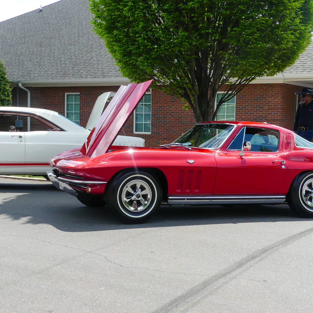 image of red car with its hood open positioned in front of a white car with a red stripe near the bottom
